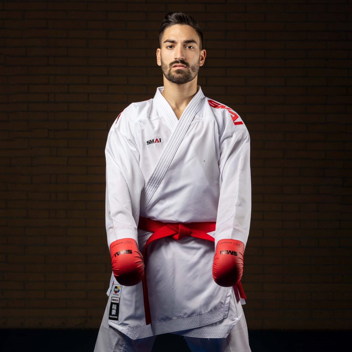 Karateka im SMAI INAZUMA Karateanzug mit rotem Gürtel und roten SMAI Faustschützern.